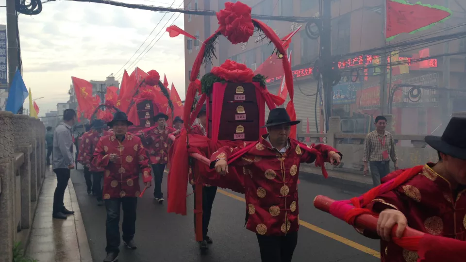 Chinese men dressed in red carrying palanquins through the village. Photo.