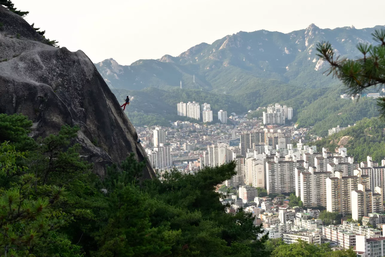 Person climbing cliff inf foreground with cityscape in background. Korea. photo.