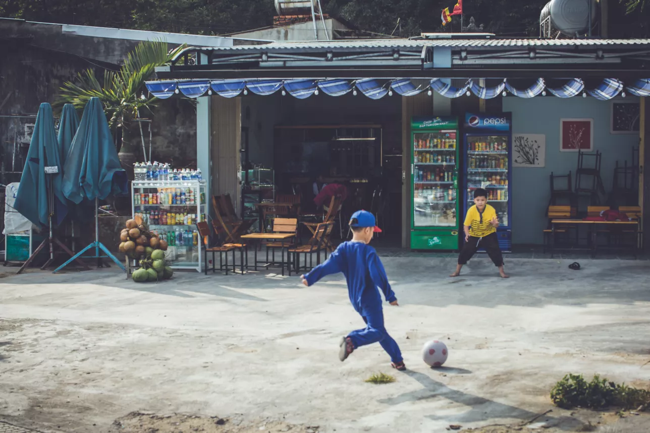 two kids playing football outside small store in Vietnam. Photo.